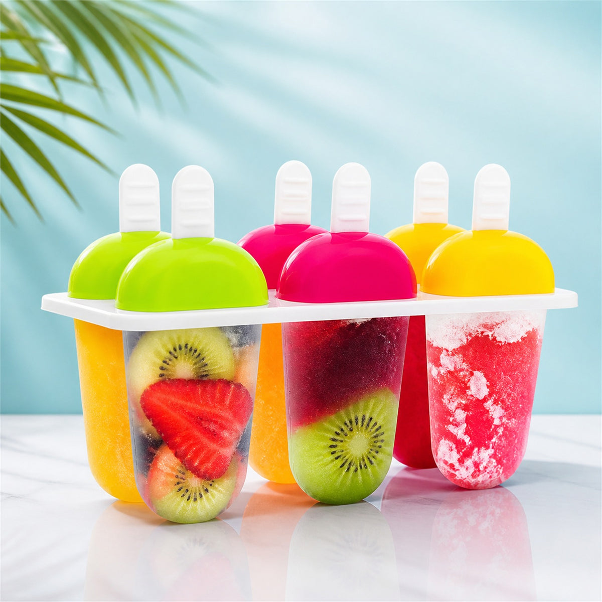 A 6-piece ice candy mold with various fruit popsicles sits on a white surface with a blue background and palm leaf.