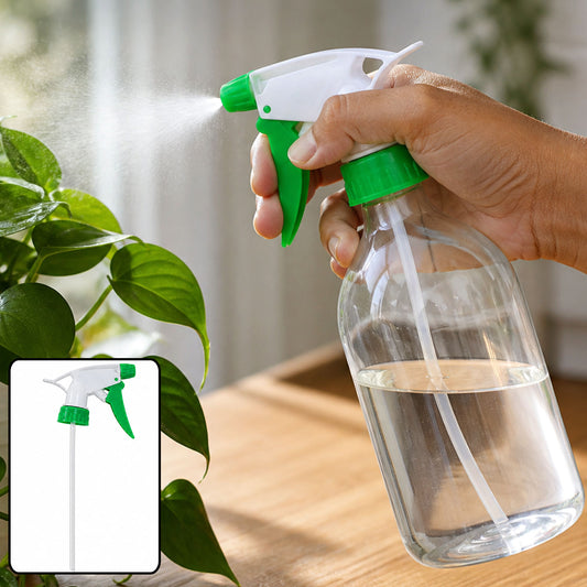 A hand holds a green and white trigger sprayer nozzle on a clear bottle, misting a green plant.