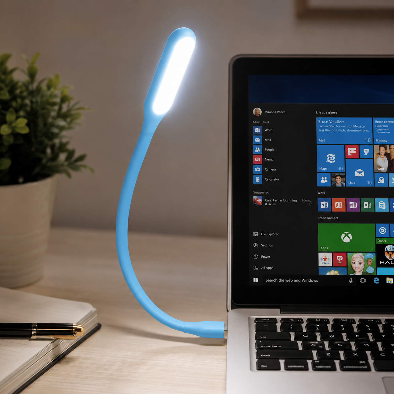 A blue flexible USB LED lamp plugged into a laptop, illuminating the keyboard and a plant pot.