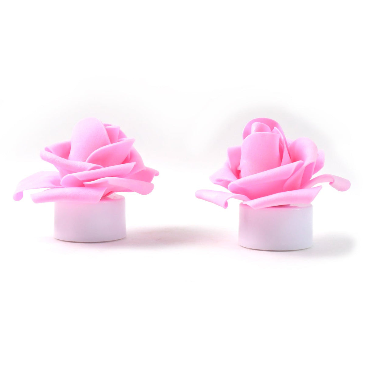 Two pink rose-shaped LED tea lights with white bases stand upright on a plain white surface.
