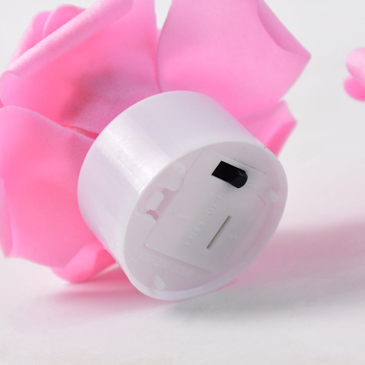 A close-up shows the white base of a pink rose LED tea light, revealing the battery compartment and switch.