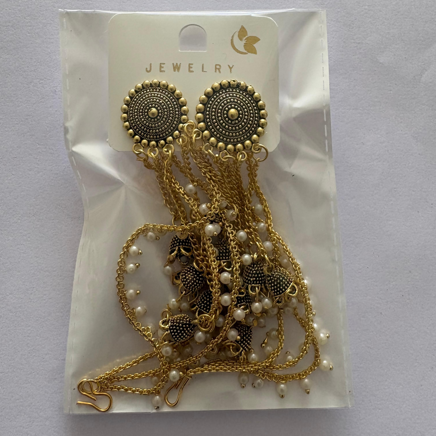 Gold tone jhumka earrings with pearl drops and chains against a subtle background