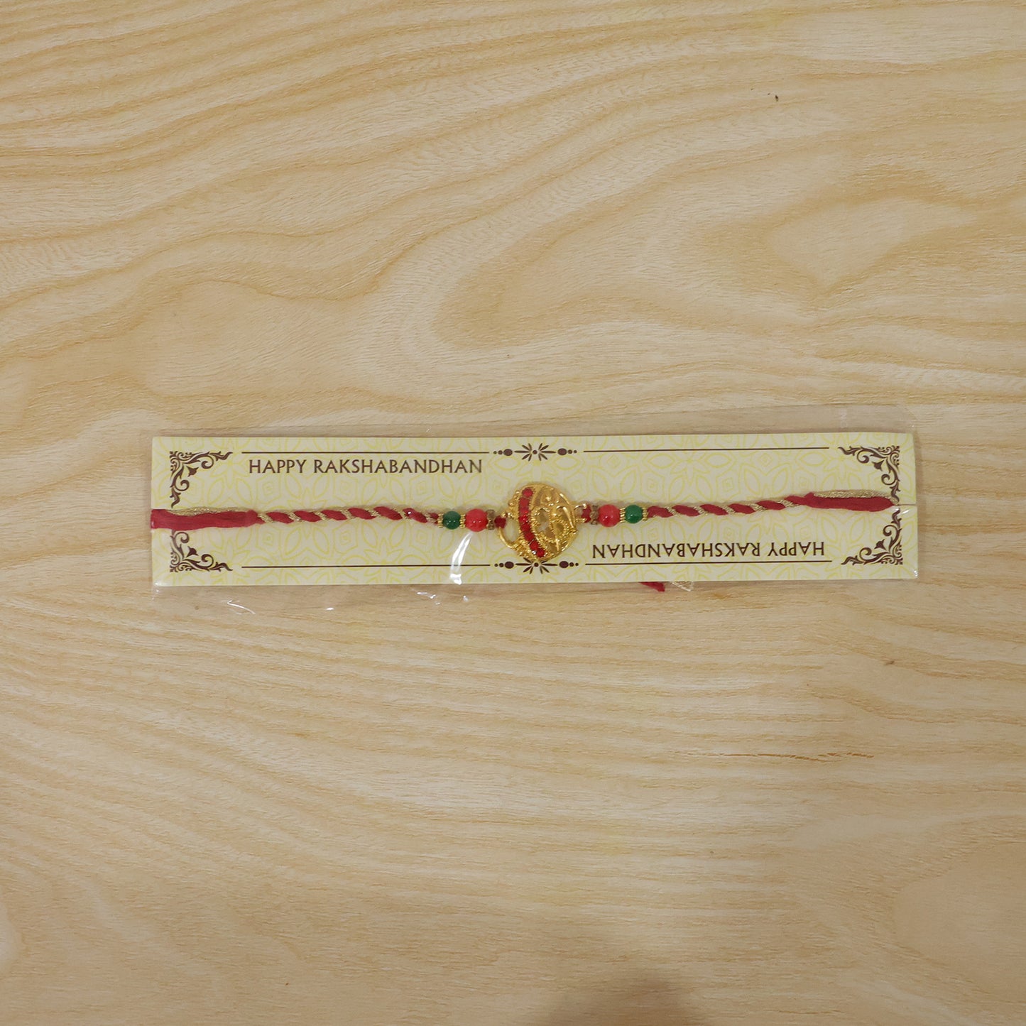 Golden Red Diamond Om Trishul Rakhi with Green Beads and Twisted Thread