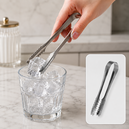 A hand uses a silver tong to place an ice cube into a glass filled with ice cubes on a white marble surface.