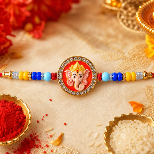 A red, yellow, and blue beaded bracelet with a round Ganesh charm lies on a cream cloth with red flowers and gold bowls.