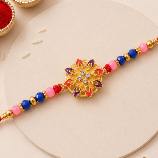 A gold and enamel floral charm with clear stones is centered on a red thread with pink, blue, and gold beads.