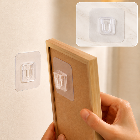 A hand holds a wooden frame, aligning its back with a transparent self-adhesive hook on a light wall.