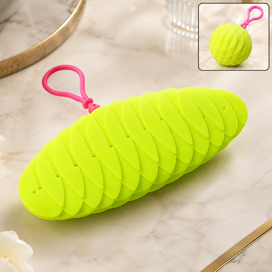 A bright green collapsible silicone ball keychain with a pink loop, shown partially collapsed on a marble surface
