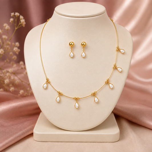 Golden necklace with teardrop pearl charms and matching earrings displayed on a cream mannequin.