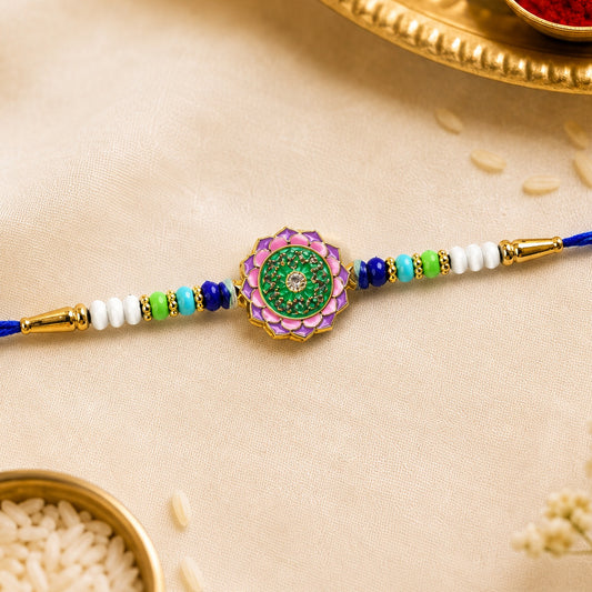 A blue rakhi with a central pink and green floral stone, flanked by white, green, and blue beads.