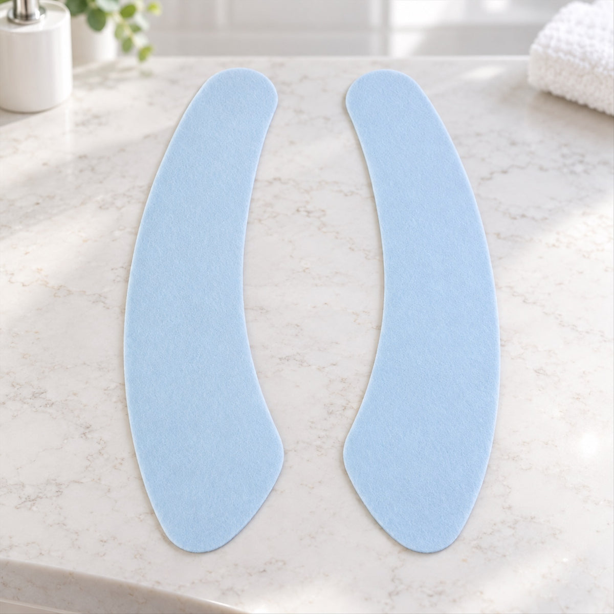 Two light blue, curved fabric pads are arranged on a white marble countertop in a bathroom.