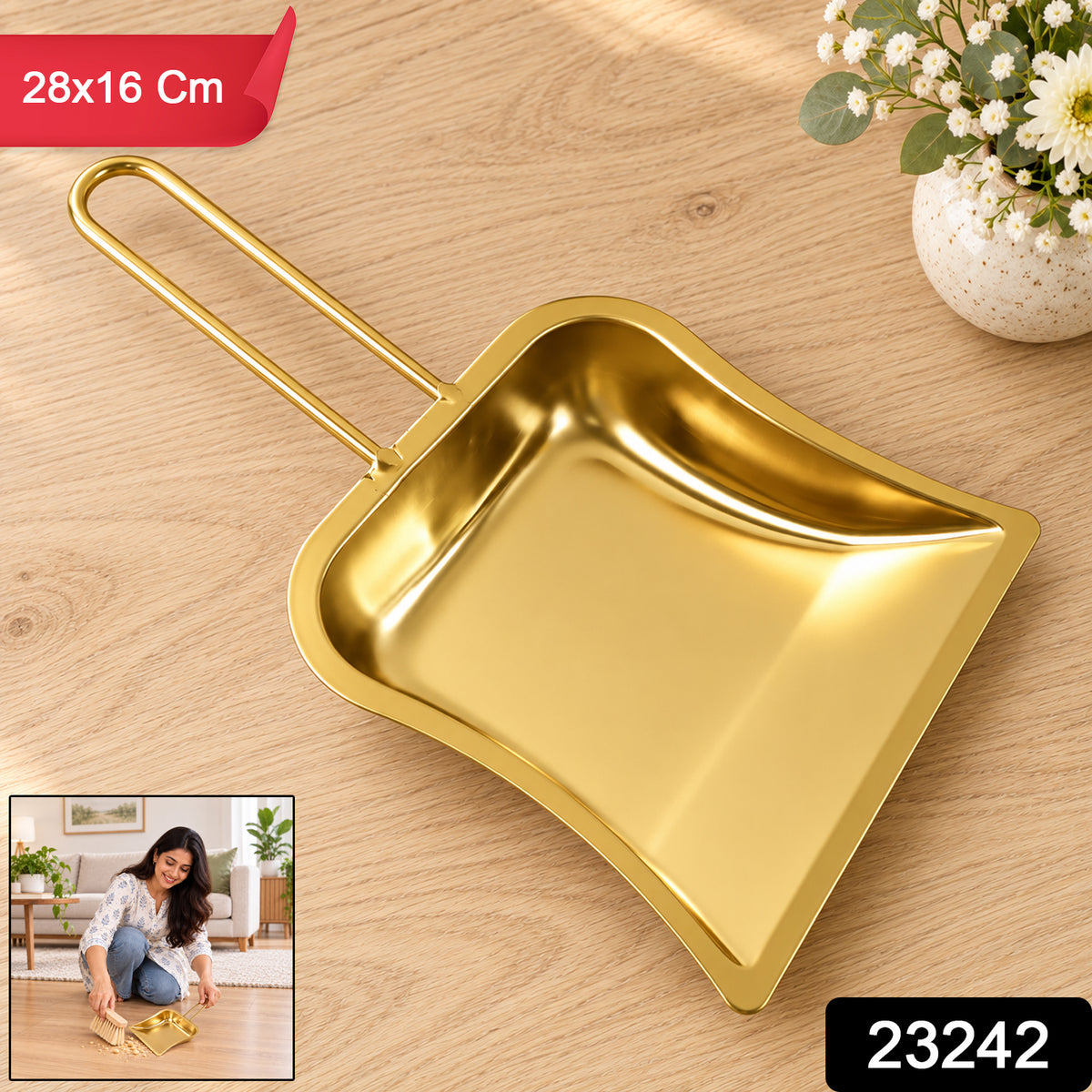 A gold-toned metal dustpan with a loop handle sits on a light wooden surface, with a small inset image of a woman using it.