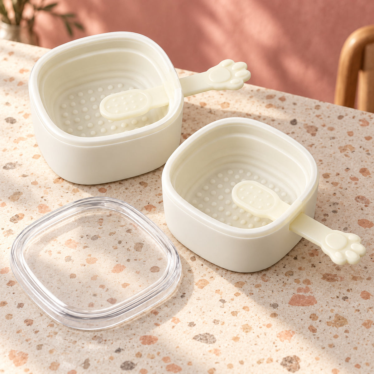 Two empty white square silicone molds with paw-shaped sticks and a clear lid sit on a speckled countertop.