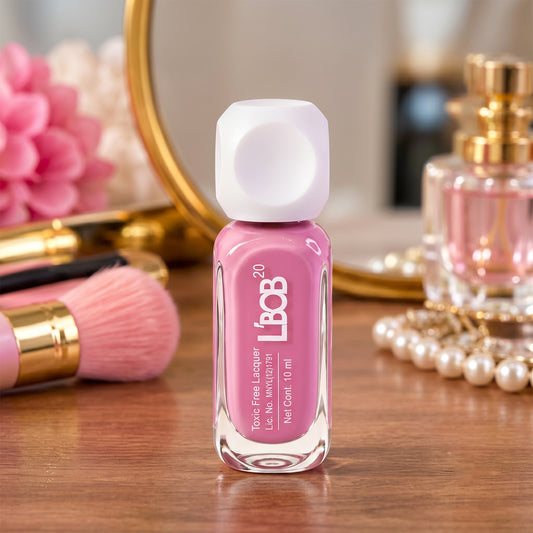 A pink nail polish bottle with a white cap stands on a wooden surface, surrounded by makeup brushes and a mirror.