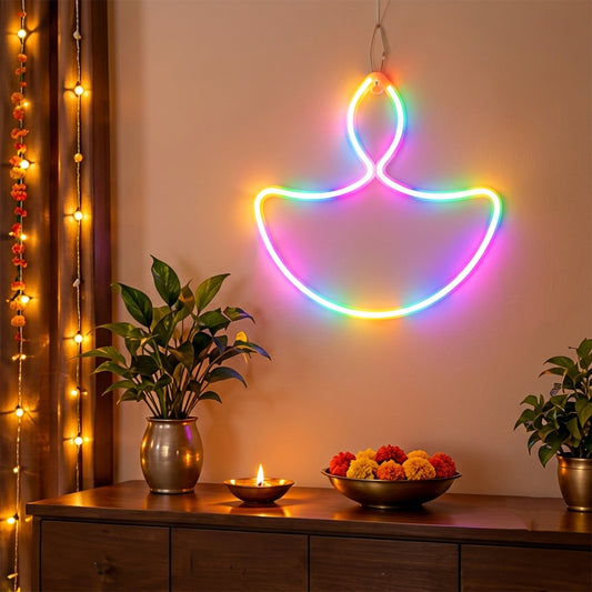 A vibrant LED diya-shaped neon light glows with multiple colors on a wall above a wooden console table with plants and a lit