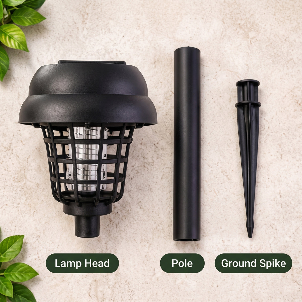 The three disassembled parts of the black solar lamp, head, pole, and spike, are laid on a textured surface with green