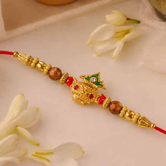 Golden Kalash Rakhi with intricate Moti work and a red thread, displayed on a traditional background.
