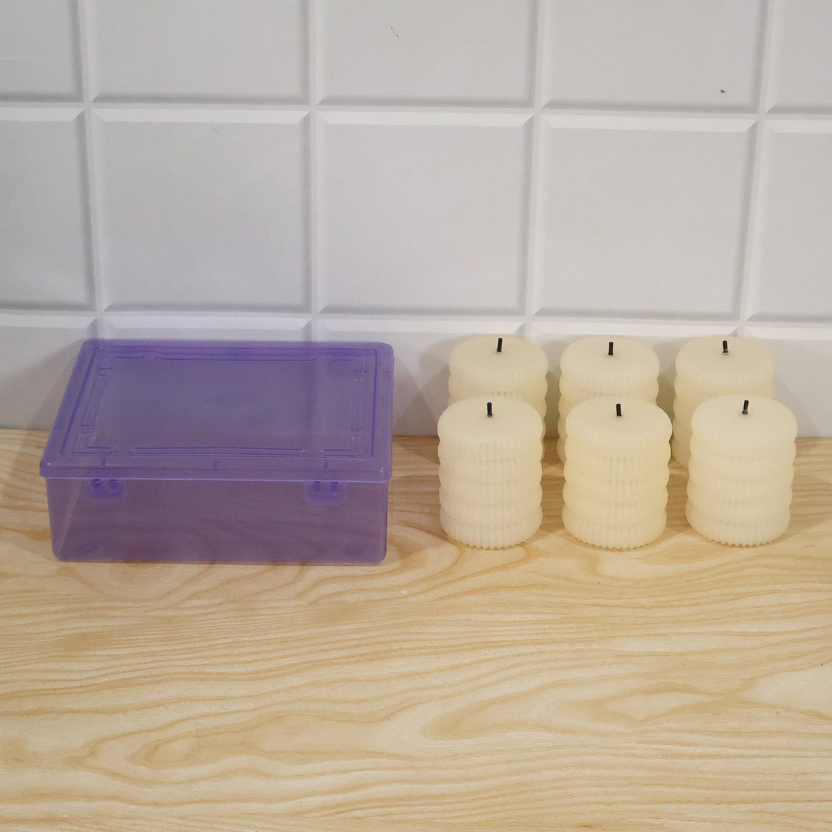 Six unlit cream-colored ribbed flameless LED tealight candles next to a translucent purple storage box.