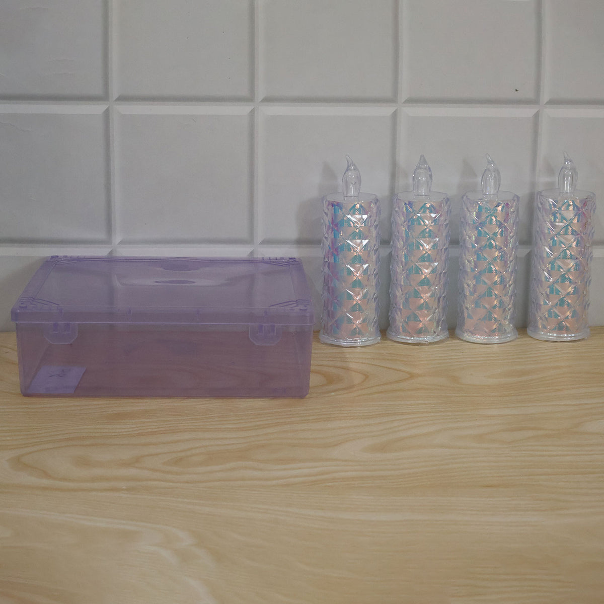 Four unlit crystal LED candles and a closed purple storage box are arranged on a light wooden surface against a white tiled