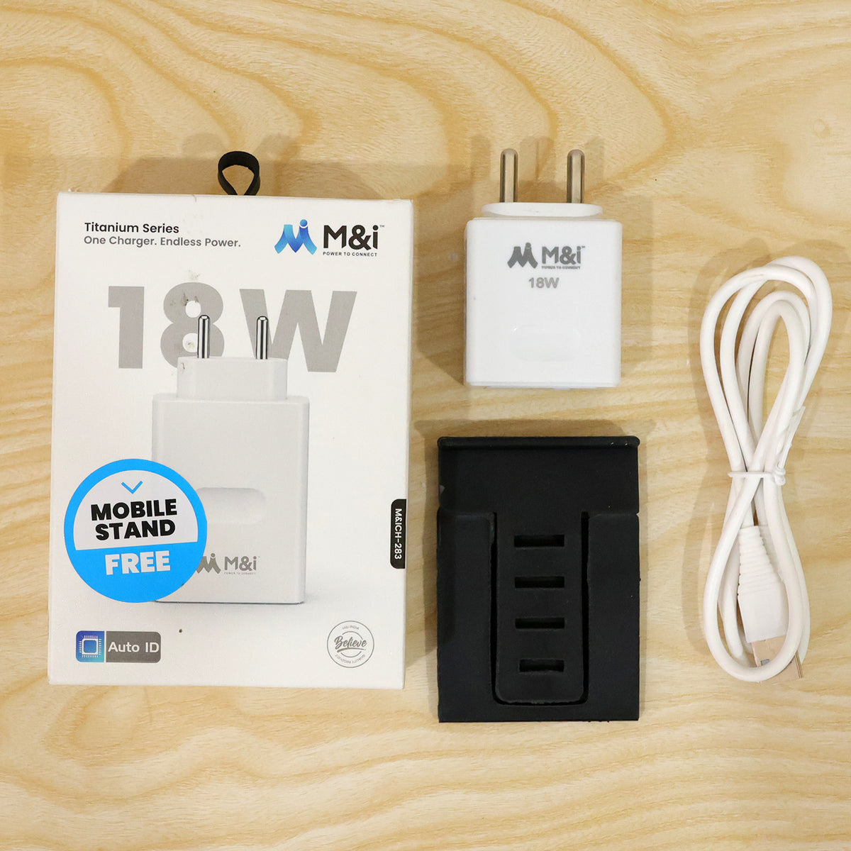 White 18W power adapter, coiled USB-A to Micro USB cable, black mobile stand, and product box on a light wood surface.