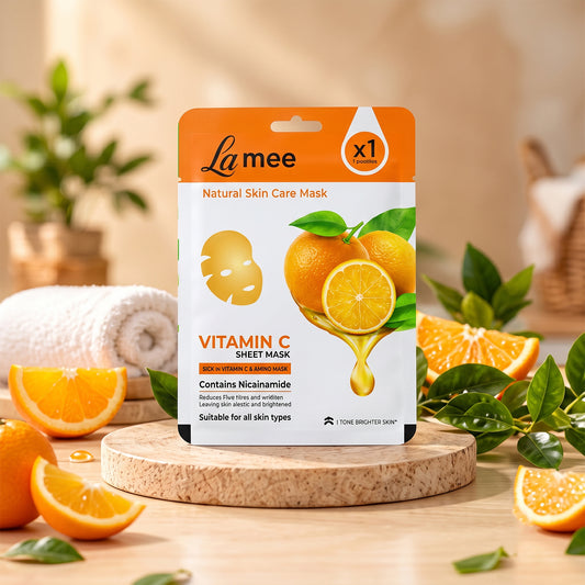 A white and orange sheet mask package stands upright on a wooden riser, surrounded by fresh orange slices and green leaves.