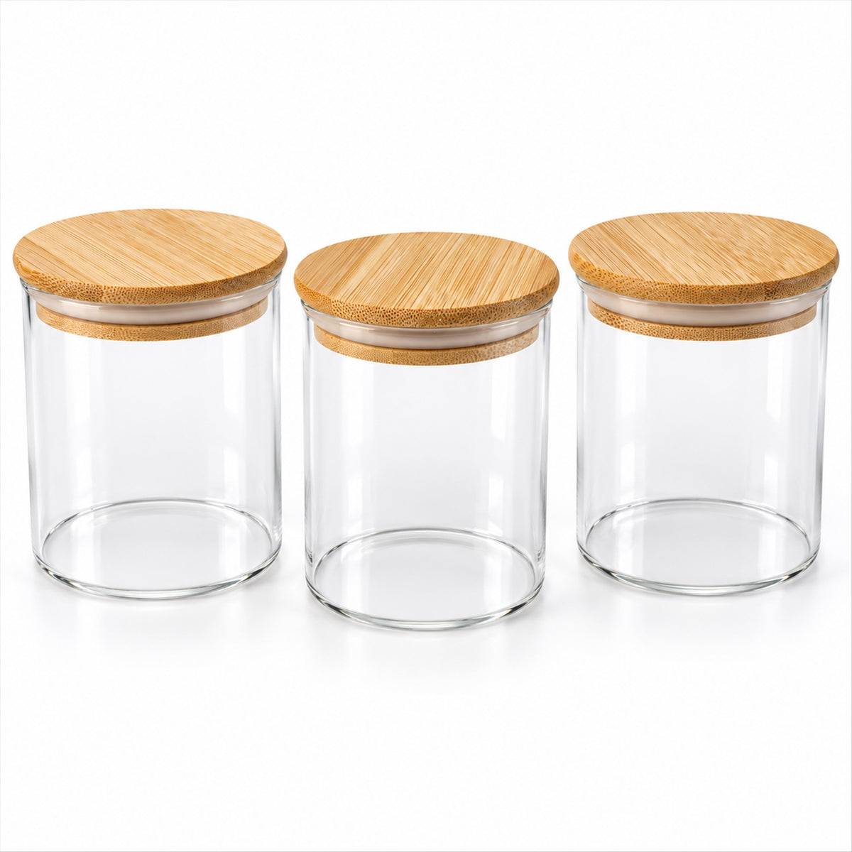 Three empty clear glass jars with light brown bamboo lids arranged in a row on a white surface.