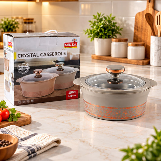 A gray insulated casserole dish with a clear lid and copper knob sits on a marble counter next to its product box.
