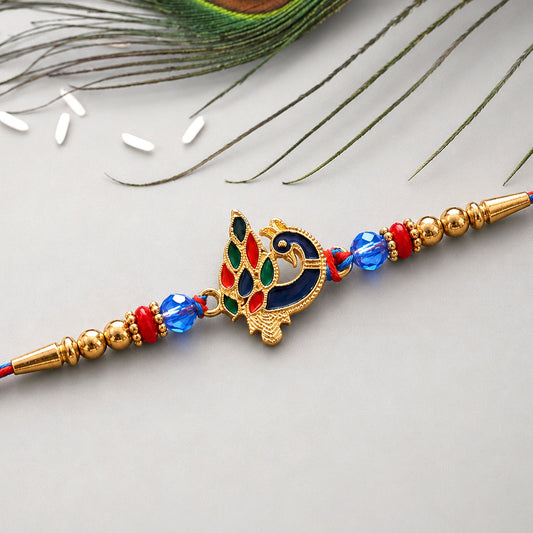 A gold peacock charm with red, green, and blue enamel details, flanked by gold beads and blue and red glass beads, on a blue