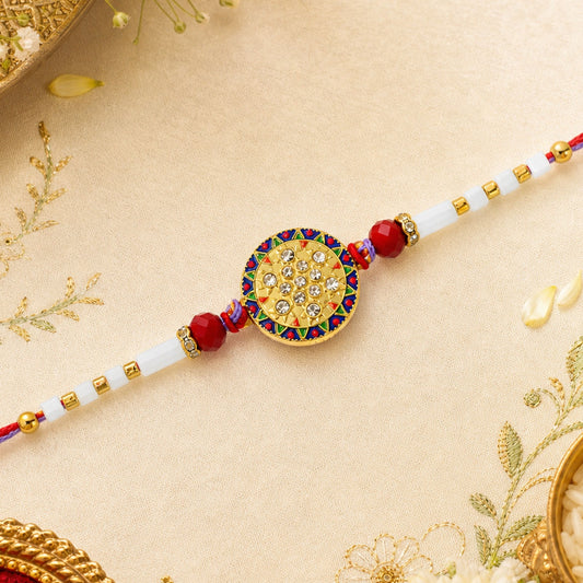 A gold, red, and white beaded bracelet with a round, ornate centerpiece featuring clear stones, on a light gold fabric.