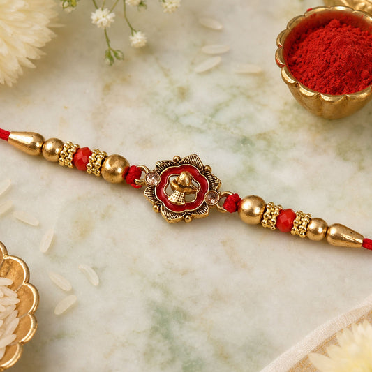 A red and gold beaded bracelet with a central flower-shaped charm, on a marble surface with rice grains and a small bowl of