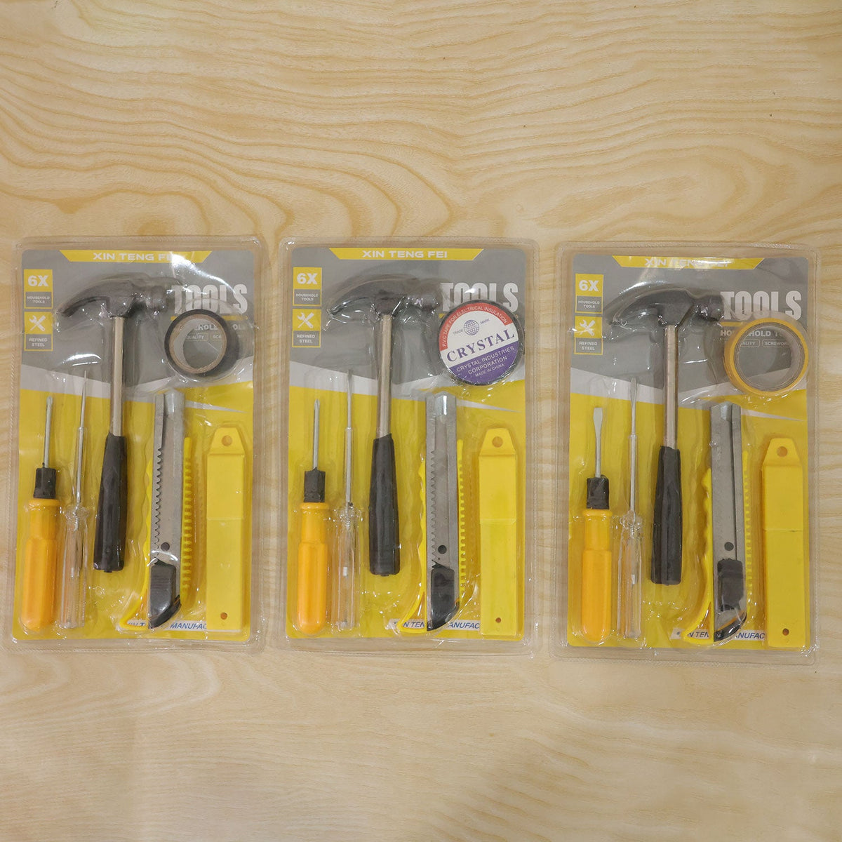 Three identical 6-in-1 household tool kits, each sealed in clear plastic packaging, are laid flat on a light wood grain