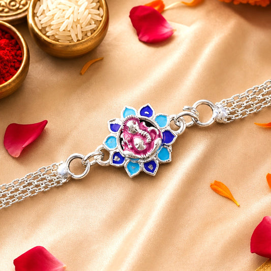 A silver chain bracelet with a pink Ganesha charm surrounded by blue and light blue enamel petals rests on a golden fabric