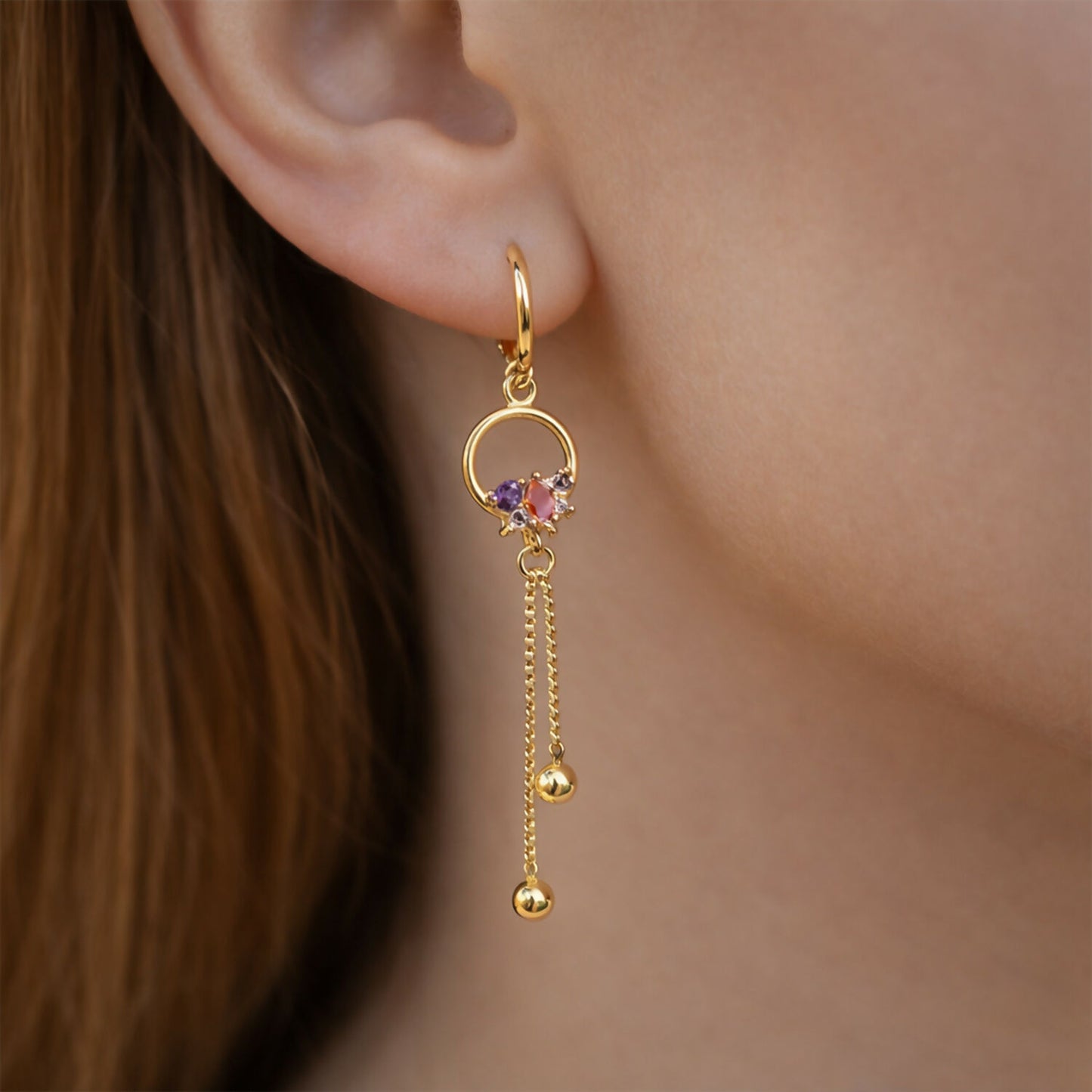 Close-up of gold finish circle drop earrings showing multicolor stone accents and delicate chain tassels