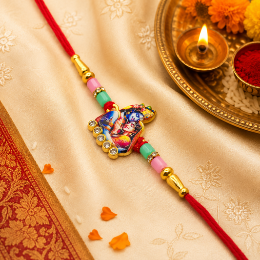 A red thread with a golden charm featuring Radha Krishna, rhinestones, and pastel beads, on a gold silk cloth with a lit