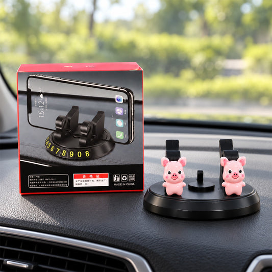 Black phone holder with two pink pig figurines and a red box on a car dashboard, showing a parking plate with numbers.