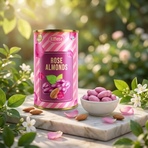 A pink tin of rose almonds stands on a marble slab with loose almonds, rose petals, and a bowl of pink almonds, surrounded