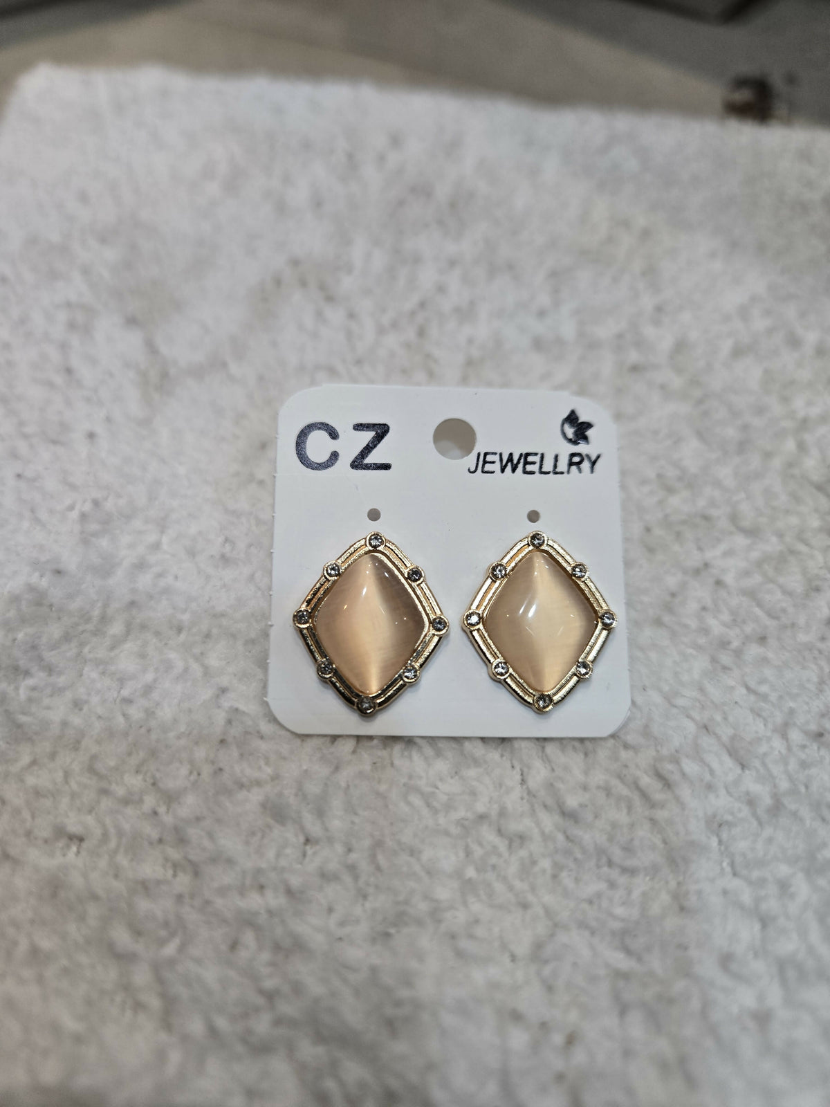 A pair of champagne geometric stud earrings with gold-tone frames and clear stone accents on a white jewelry card.