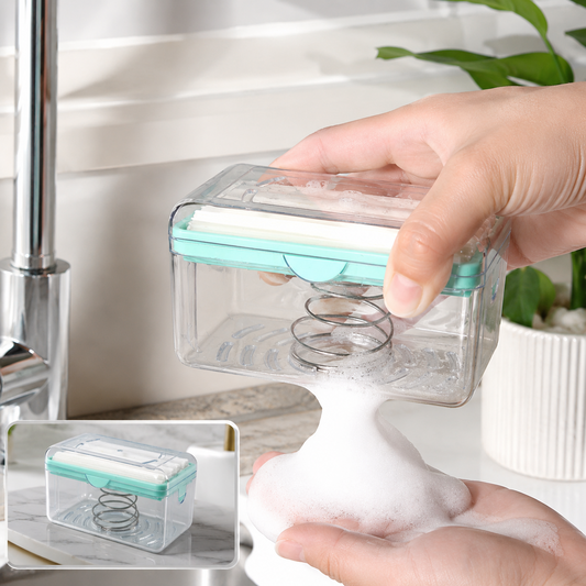 A hand holds a clear soap dispenser with a mint green top over a sink, creating foam in the other hand.