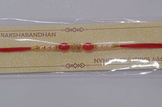 Traditional pearl and red beaded Rakhi with golden accents displayed on woven fabric