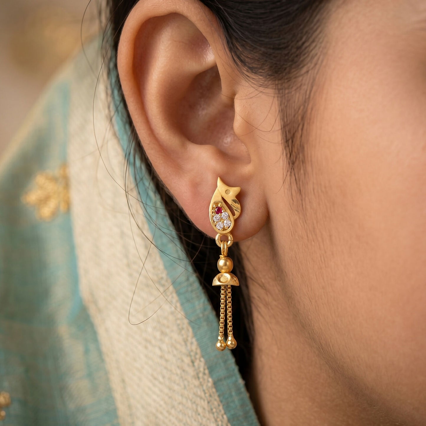 Side view of gold floral teardrop earrings with ruby accent