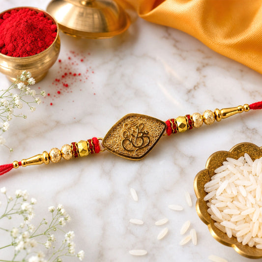 A gold-colored, leaf-shaped charm with a Ganesha symbol is centered on a red thread, flanked by gold and red beads, with