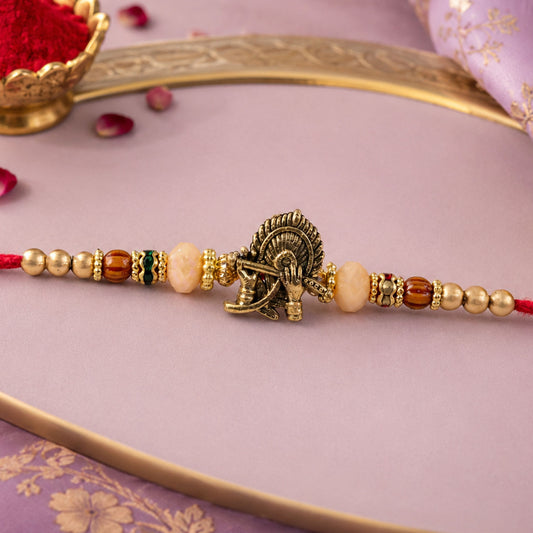 Close-up of Krishna Flute Peacock Rakhi with antique gold centre and peach beads.
