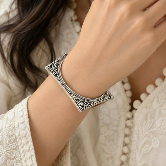 A woman wears a single square-shaped oxidized silver bangle with intricate tribal patterns on her wrist.