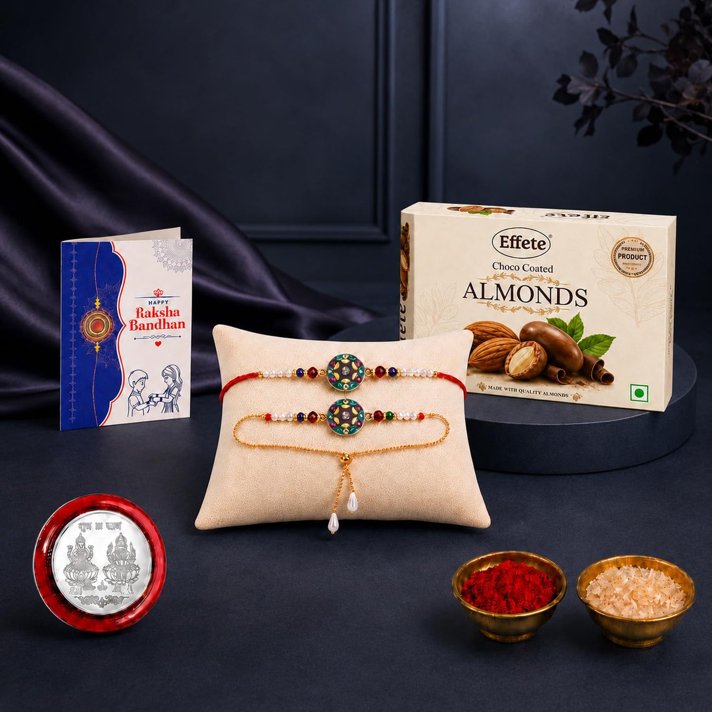 A Rakhi gift set on a dark surface features two colorful bracelets on a beige pillow, a box of chocolate almonds, a greeting