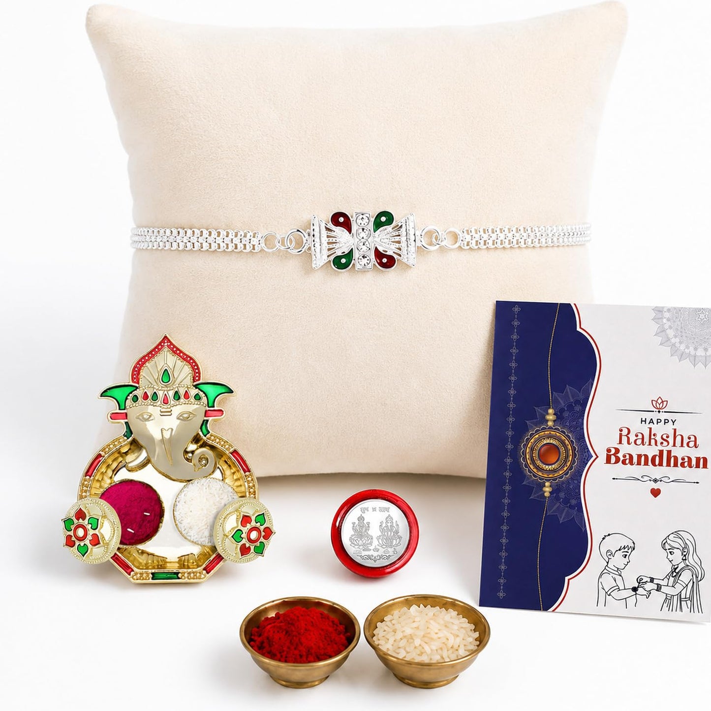 A silver bracelet with a red and green centerpiece rests on a cream pillow, next to a Ganesha pooja thali, two small bowls