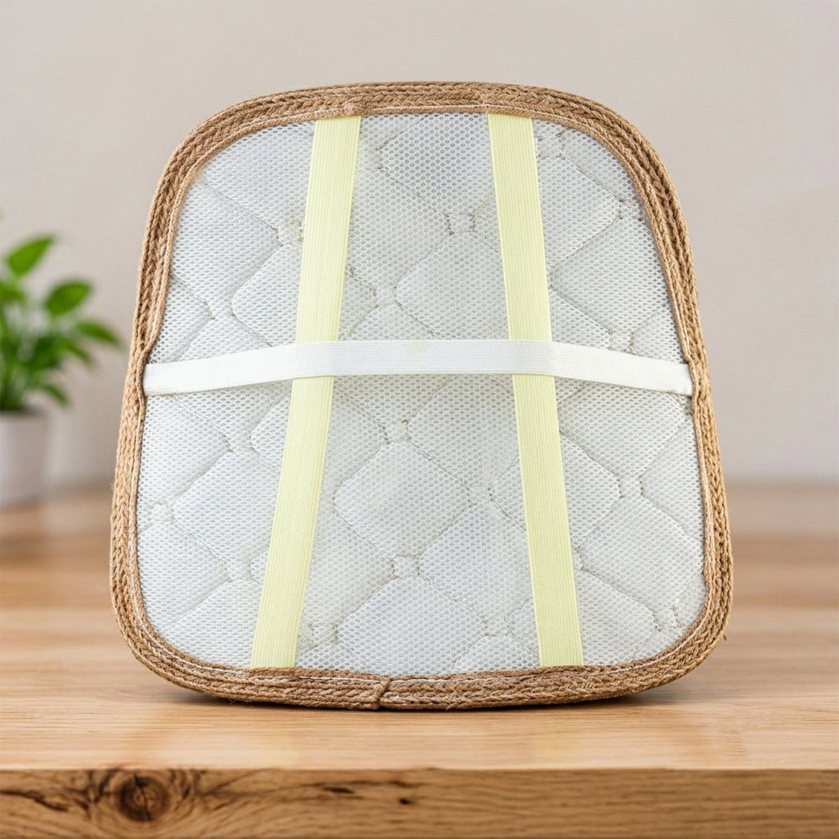 Back view of the cushion showing white mesh, yellow elastic straps, and a woven border on a wooden surface.