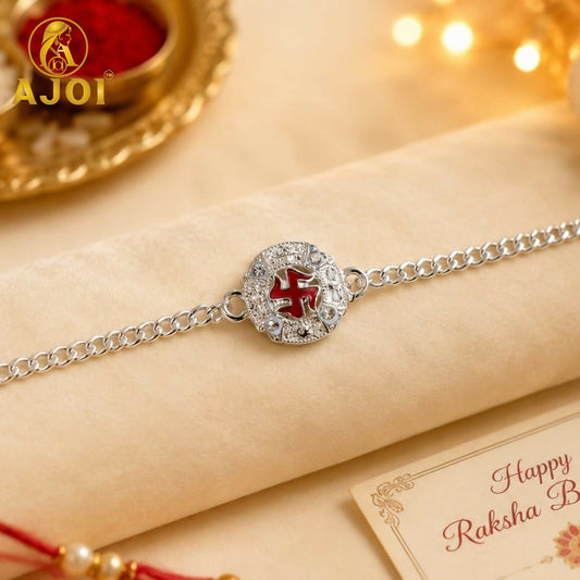 A silver chain Rakhi bracelet with a round, ornate center featuring a red Swastik symbol, resting on a light brown cloth
