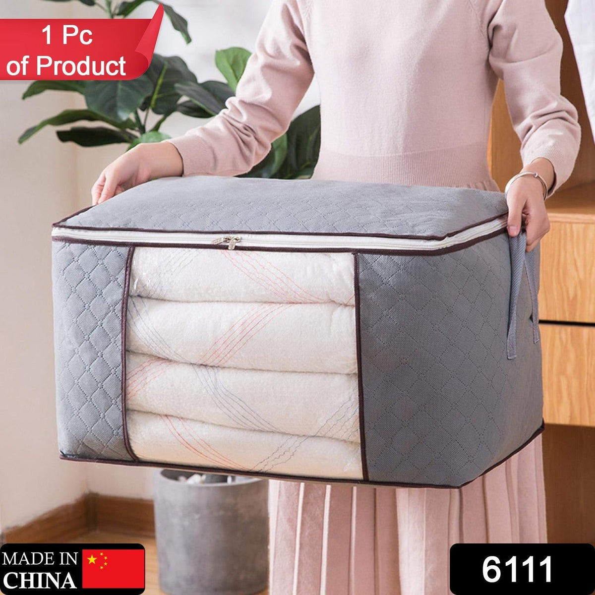 A person holds a grey quilted fabric storage bag with a clear window, filled with folded white blankets.