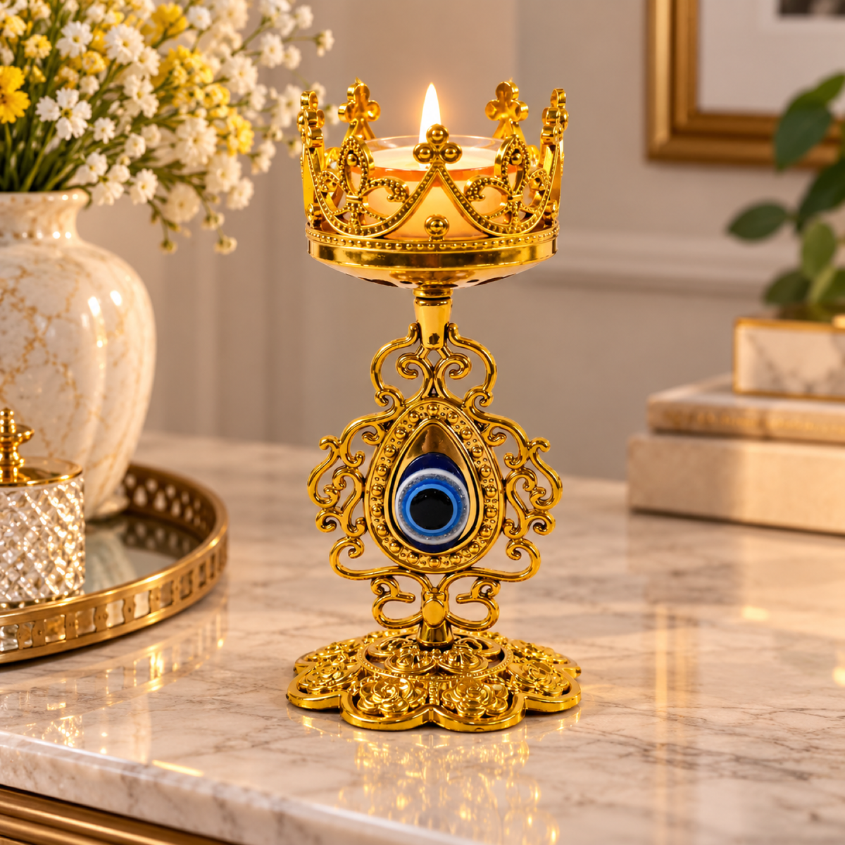 A lit candle in a gold metal holder with a crown design and a blue evil eye charm, on a marble surface.