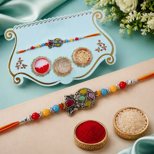 Multicolor teardrop leaf rakhi with orange thread and stone detailing.